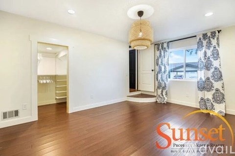 A Sunset Realty sign is displayed in a spacious, empty room with hardwood floors and a large window.