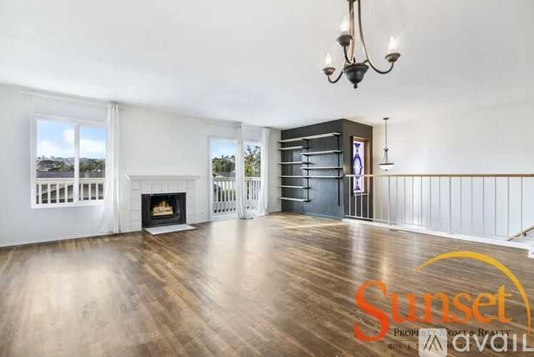 A Sunset real estate sign is displayed in a spacious living room with hardwood floors and a fireplace.