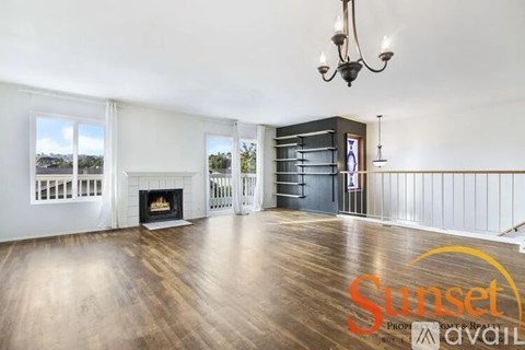 A Sunset real estate sign is displayed in a spacious living room with hardwood floors and a fireplace.