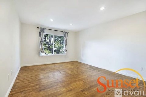 A room with wooden flooring and a window with a view of trees.