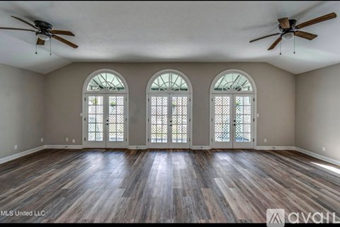 A spacious room with wood flooring and three arched windows.