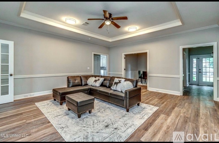 A spacious living room with a brown leather couch and a ceiling fan.
