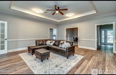 A spacious living room with a brown leather couch and a ceiling fan.