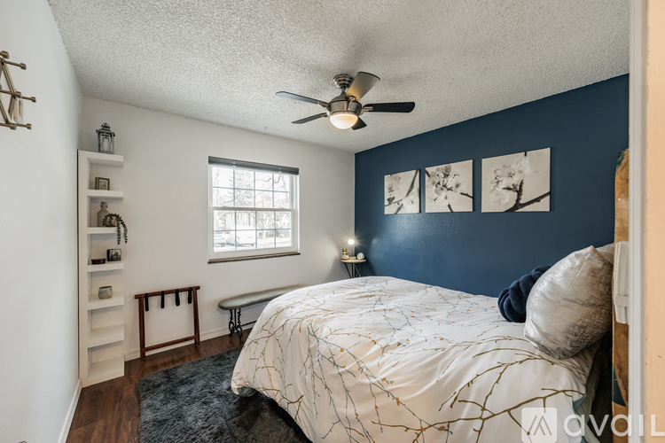A bedroom with a bed, a window, a ceiling fan, and a nightstand with a lamp.