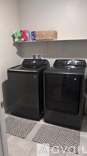 Two black ovens in a kitchen with a shelf above them.