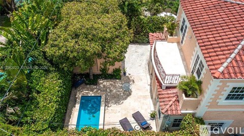 A bird's eye view of a house with a red tiled roof and a swimming pool surrounded by greenery.
