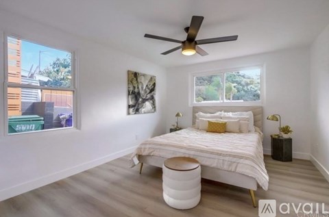 A bedroom with a bed, a ceiling fan, and a window with a view of a building.