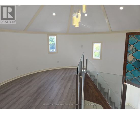 A large open space with a wooden floor and a staircase with a glass railing.