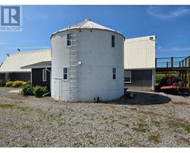 A grain silo is in the foreground with a tractor in the background.
