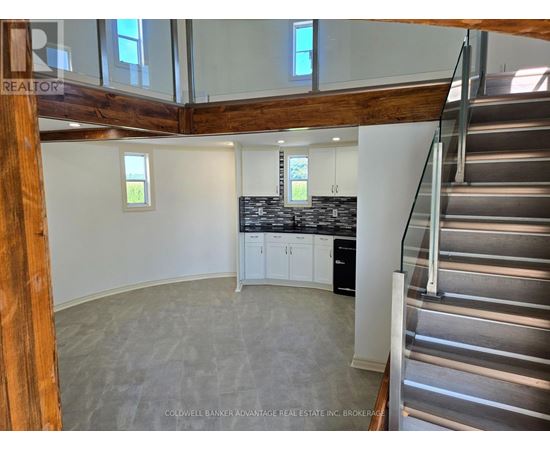 A large open space with a staircase on the right and a kitchen area with a countertop and cabinets on the left.