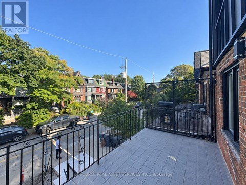 A balcony with a black railing overlooks a street with cars and houses.