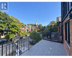 A balcony with a black railing overlooks a street with cars and houses.