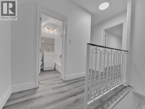 A white hallway with a staircase and a bedroom visible through the door.
