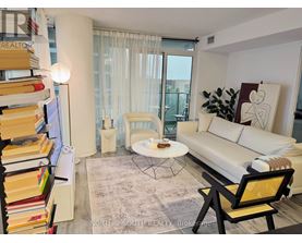 A living room with a white couch, a coffee table, a bookshelf, and a window with curtains.