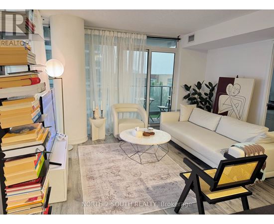 A living room with a white couch, a coffee table, a bookshelf, and a window with curtains.