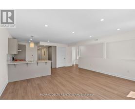 A spacious room with wooden flooring and white walls, with a bar area in the corner.