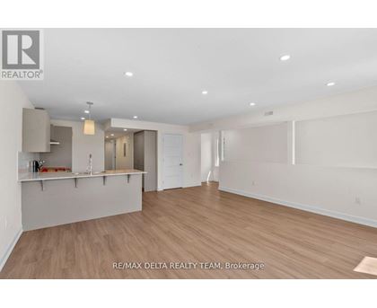 A spacious room with wooden flooring and white walls, with a bar area in the corner.