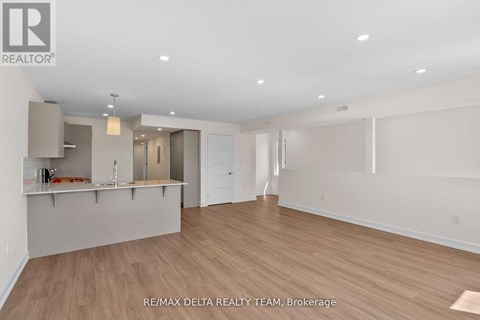 A spacious room with wooden flooring and white walls, with a bar area in the corner.