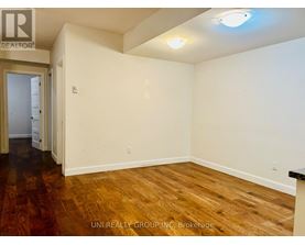 A room with wooden floors and white walls, with a door on the left and a light on the ceiling.