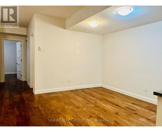A room with wooden floors and white walls, with a door on the left and a light on the ceiling.