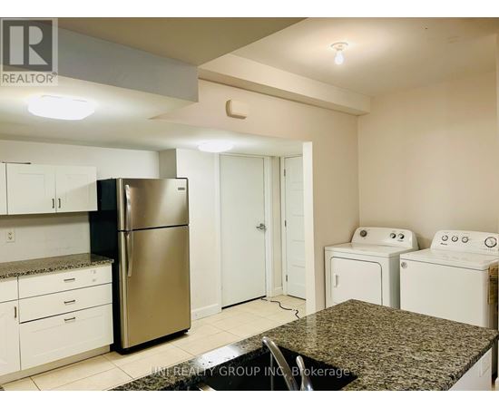 A kitchen with a stainless steel refrigerator, white cabinets, and a granite countertop.