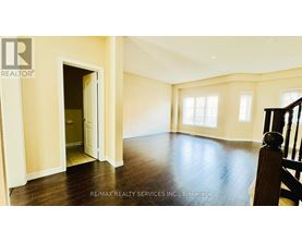 A spacious room with wooden floors and a staircase on the right side.