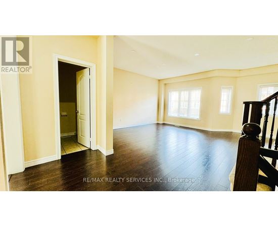 A spacious room with wooden floors and a staircase on the right side.