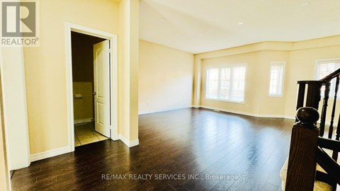 A spacious room with wooden floors and a staircase on the right side.
