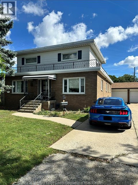 A blue car is parked in front of a two-story house.
