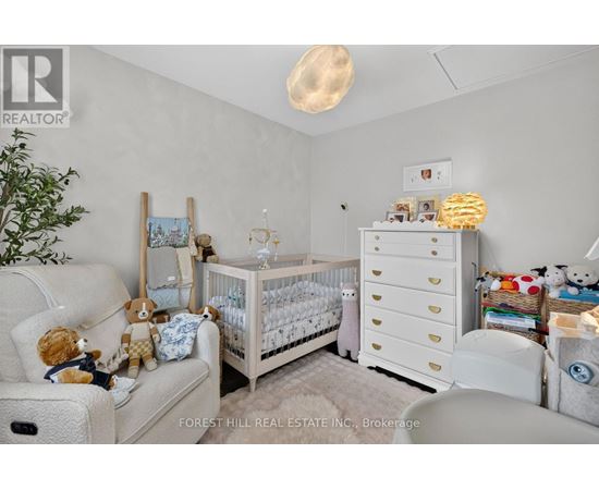 A baby nursery with a white crib, a changing table, and a teddy bear on the couch.