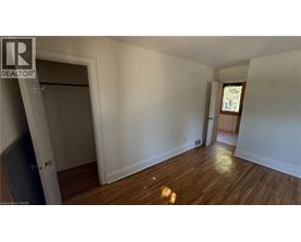 A room with wooden floors and white walls, with a door on the left and a window on the right.