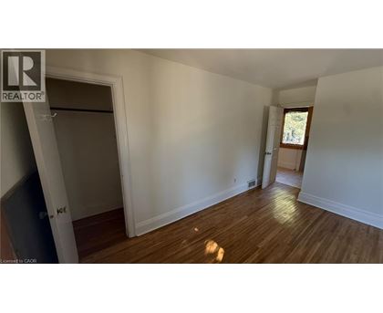A room with wooden floors and white walls, with a door on the left and a window on the right.