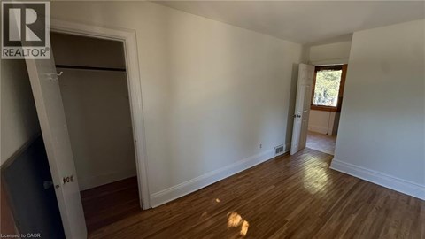 A room with wooden floors and white walls, with a door on the left and a window on the right.