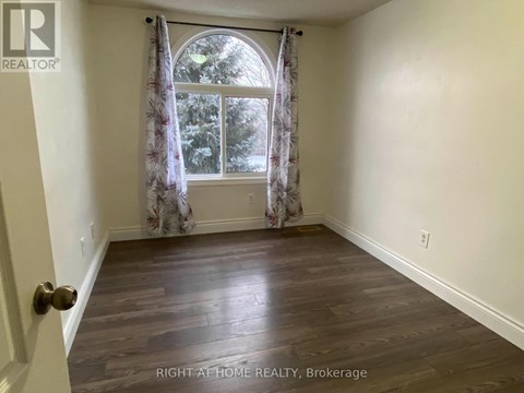 A room with wooden flooring and a window with curtains.