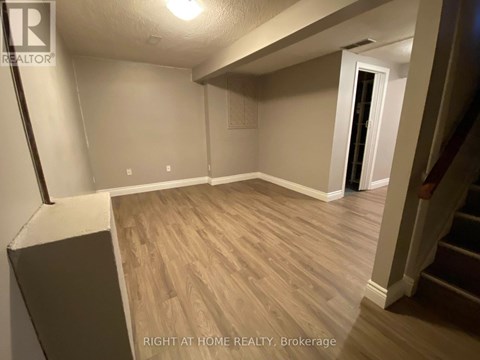 A room with wooden flooring and a staircase leading to another room.