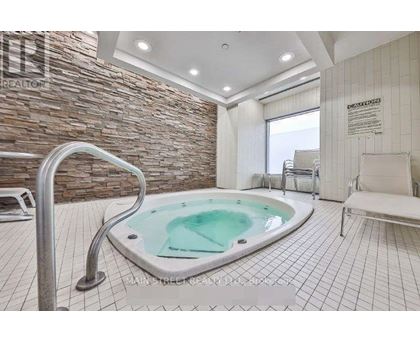 A hot tub sits in the middle of a tiled room with a stone wall.