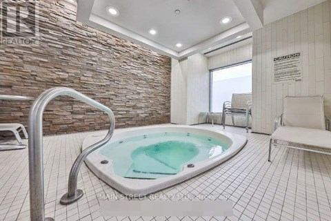 A hot tub sits in the middle of a tiled room with a stone wall.