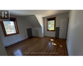 A room with wooden floors and white walls, with a window on the left side.