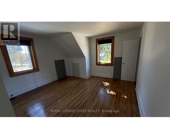 A room with wooden floors and white walls, with a window on the left side.