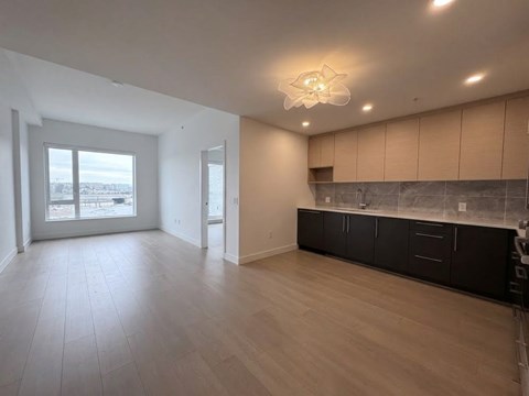 A spacious room with wooden floors and a kitchen area with black cabinets.