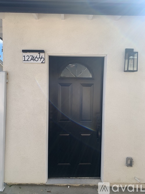 A black door with a glass window above it is on a white wall with a black lantern to the right.