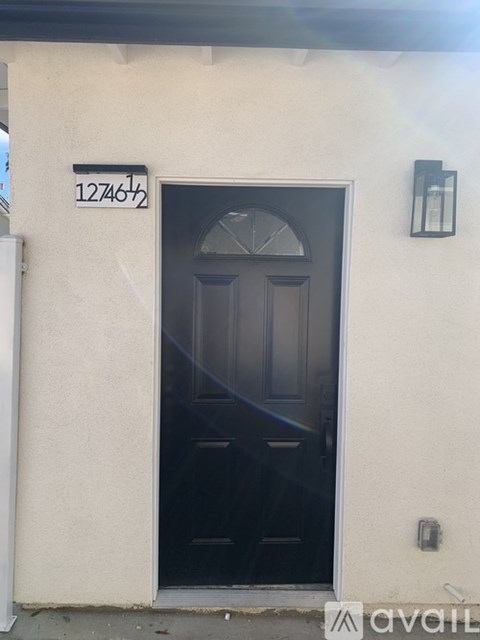 A black door with a glass window above it is on a white wall with a black lantern to the right.