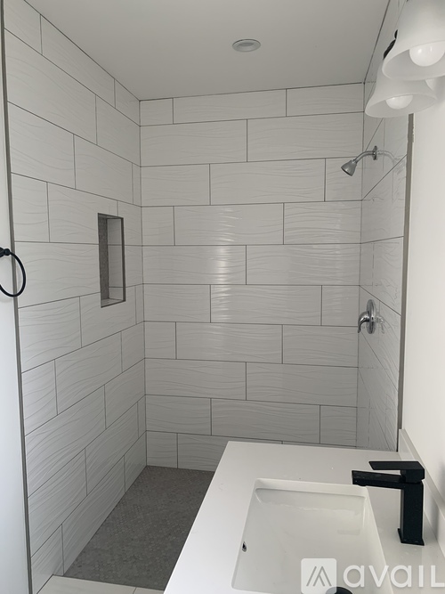 A white tiled bathroom with a white sink and a shower head.