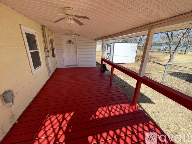 A porch with red flooring and a ceiling fan.