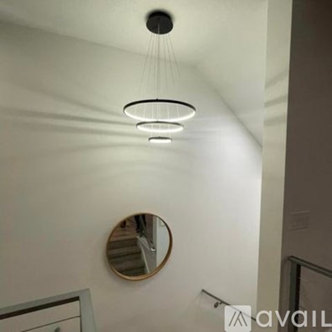 A modern chandelier with three lights is hanging from the ceiling in a room with a round mirror on the wall.