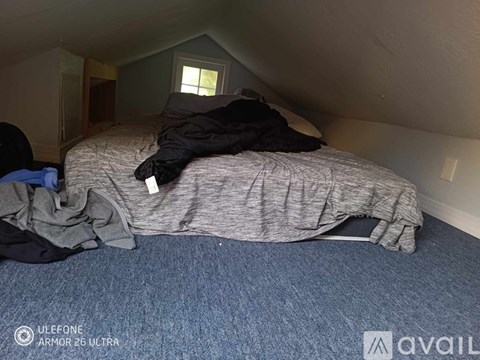 A bed with a grey blanket and a black jacket on it.