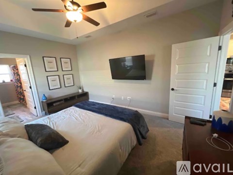 A bedroom with a bed, a ceiling fan, and a flat screen TV mounted on the wall.