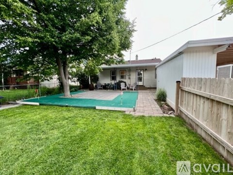 A backyard with a green lawn, a tree, a pool, and a house.