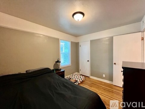 A bedroom with a bed, a nightstand with a lamp, and a window with a view of a building outside.