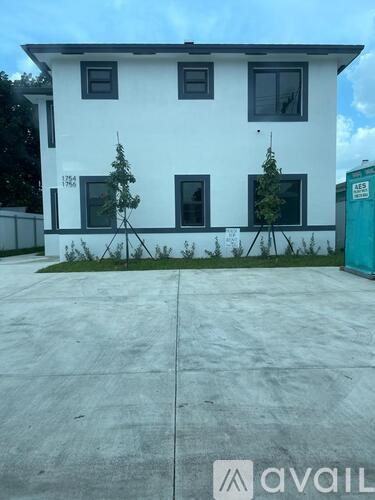 A white house with a black roof and a green container in the background.